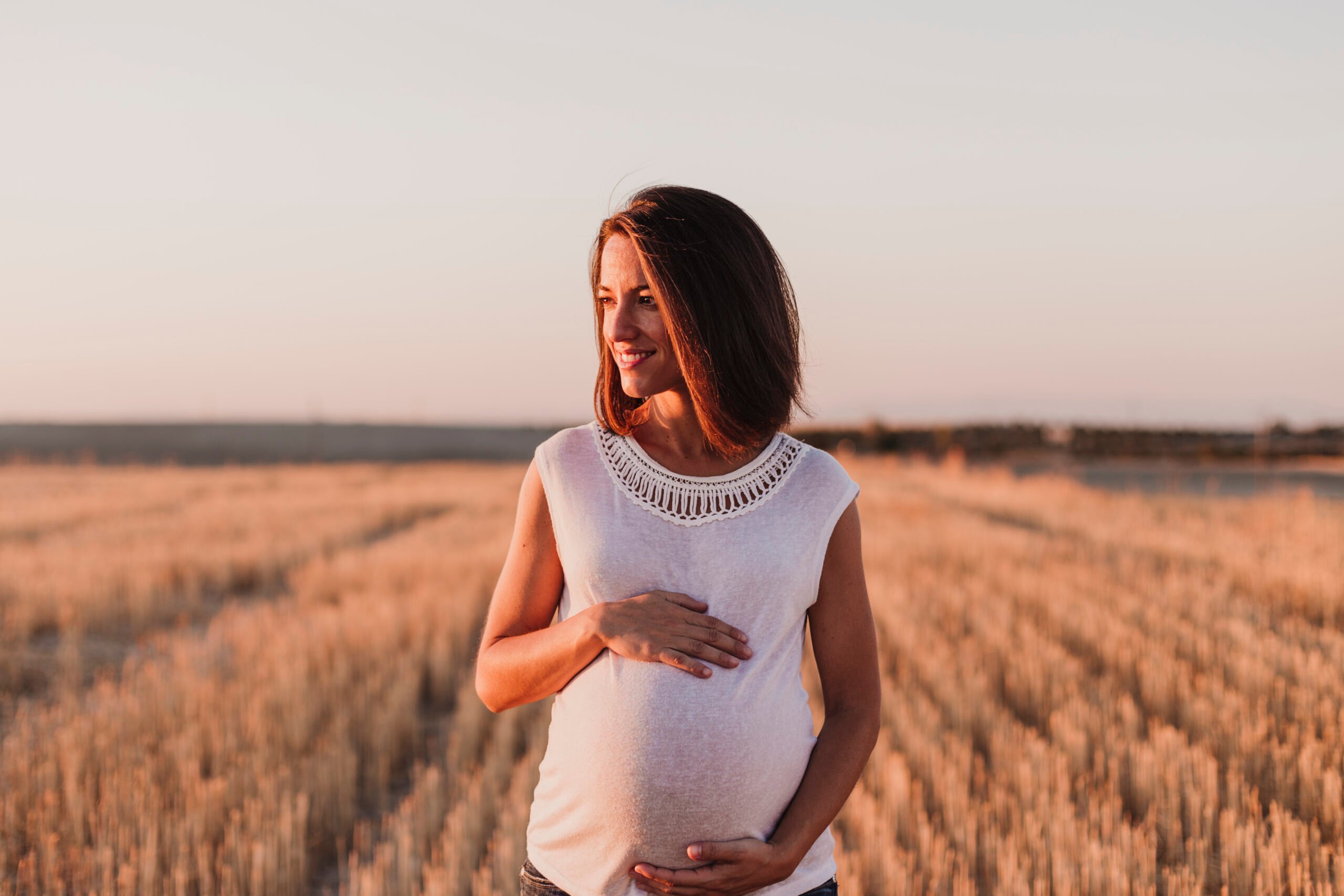 portrait outdoors of a young beautiful pregnant woman touching her belly while expecting a baby. Outdoors lifestyle. Yellow background
